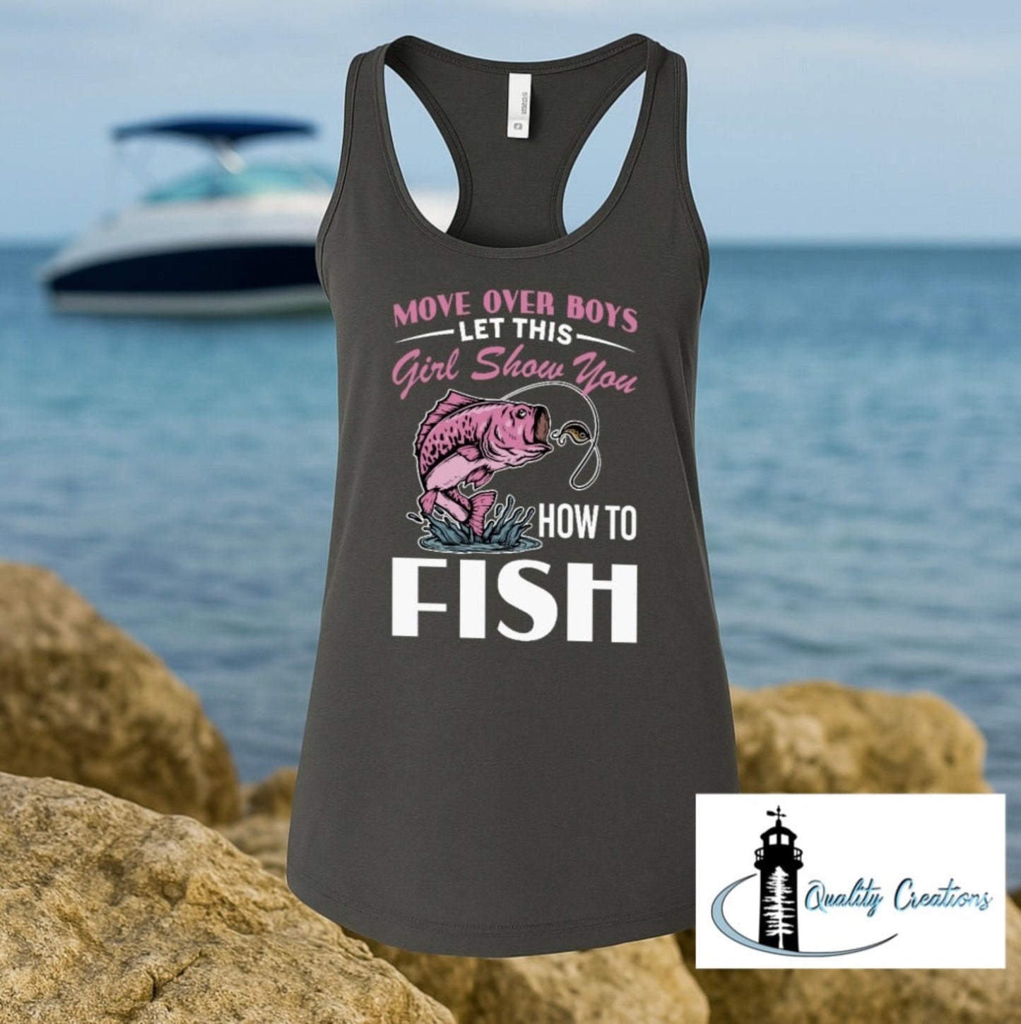 Black ladies racerback tank top with a pink and white fishing graphic that says Move Over Boys Let This Girl Show You How to Fish, shown on a beach background with a Quality Creations logo in the corner.