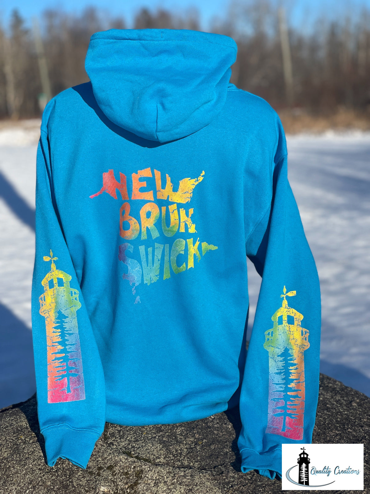 Sapphire blue New Brunswick hoodie with rainbow New Brunswick back design and lighthouse sleeve graphics, custom East Coast apparel from New Brunswick.