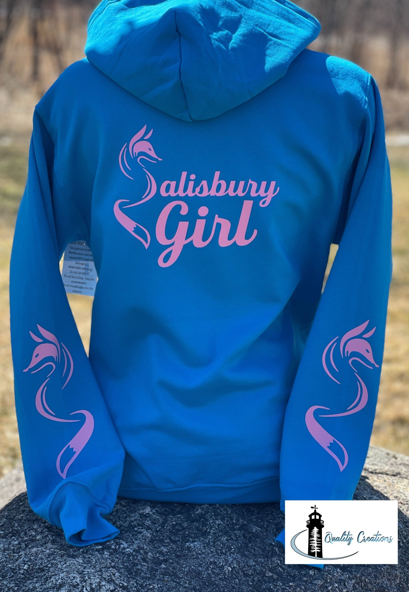 Sapphire blue Salisbury Girl pullover hoodie with hot pink text and fox sleeve graphics. A vibrant design for proud locals from Salisbury, Moncton, Sussex, and Hampton, New Brunswick.