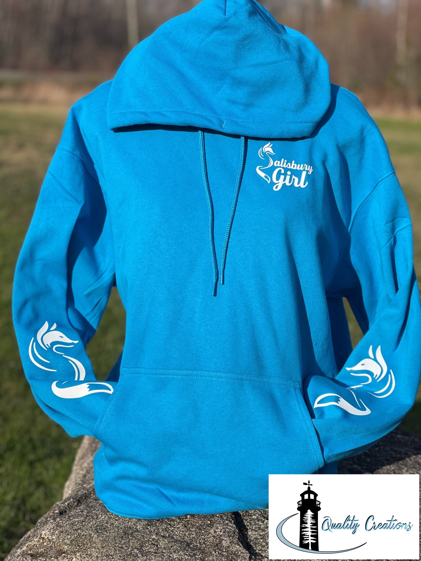 Sapphire blue Salisbury Girl pullover hoodie with white text and fox sleeve graphics. Designed in Salisbury, New Brunswick—home of the Silver Fox.