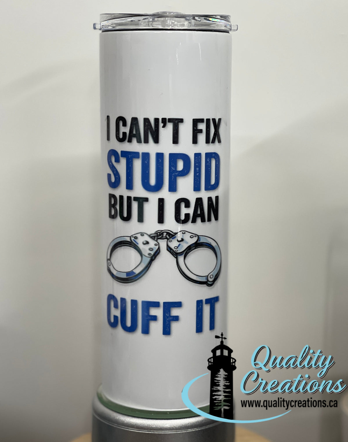 A white insulated tumbler with a clear lid featuring the printed text 'I CAN'T FIX STUPID BUT I CAN CUFF IT' in black and blue, alongside a handcuff graphic. A 'Quality Creations' watermark is visible in the lower right corner.