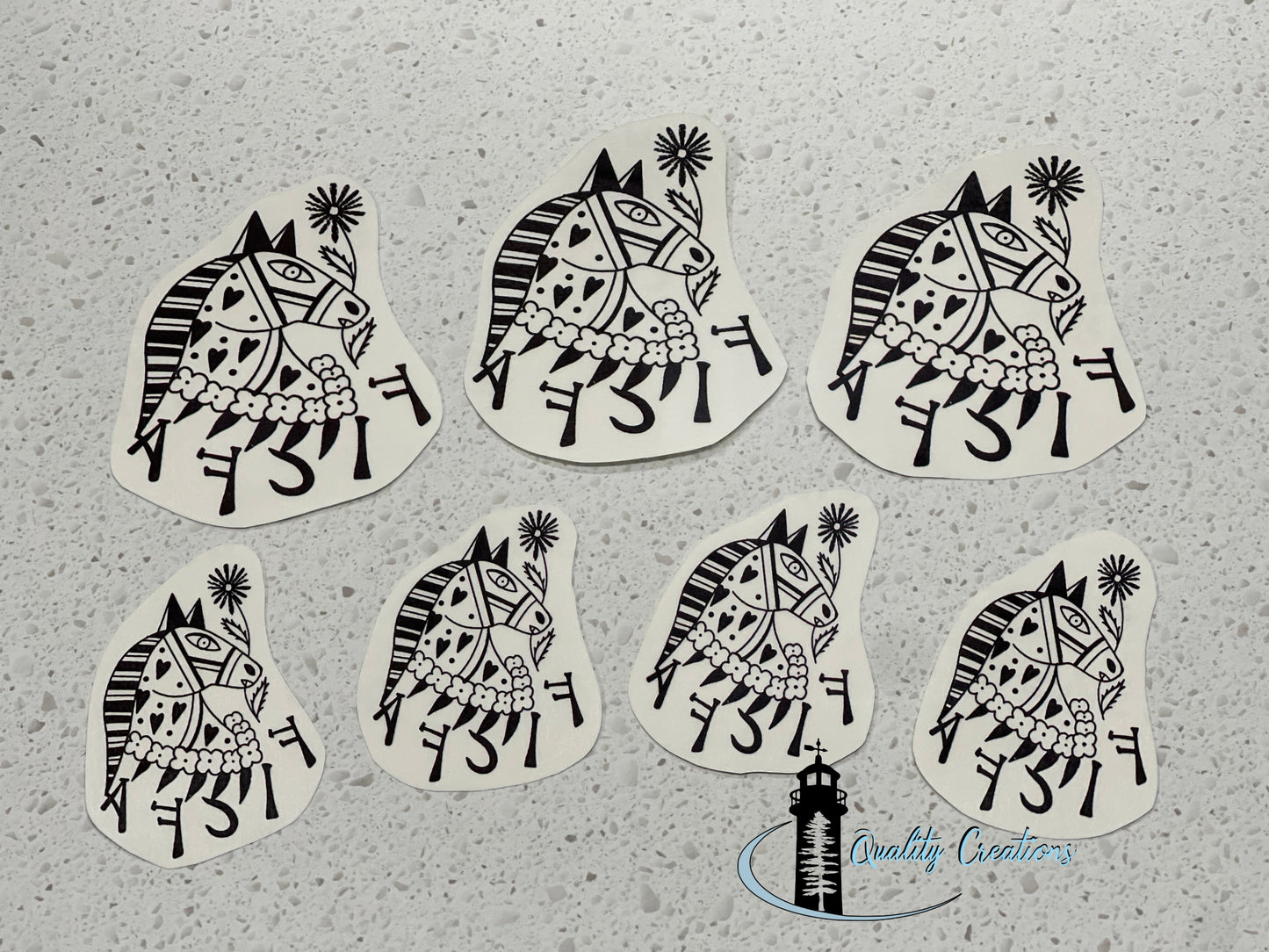 Seven die-cut stickers featuring a black and white hand-drawn style illustration of a horse with Hebrew lettering, arranged on a light gray speckled surface.