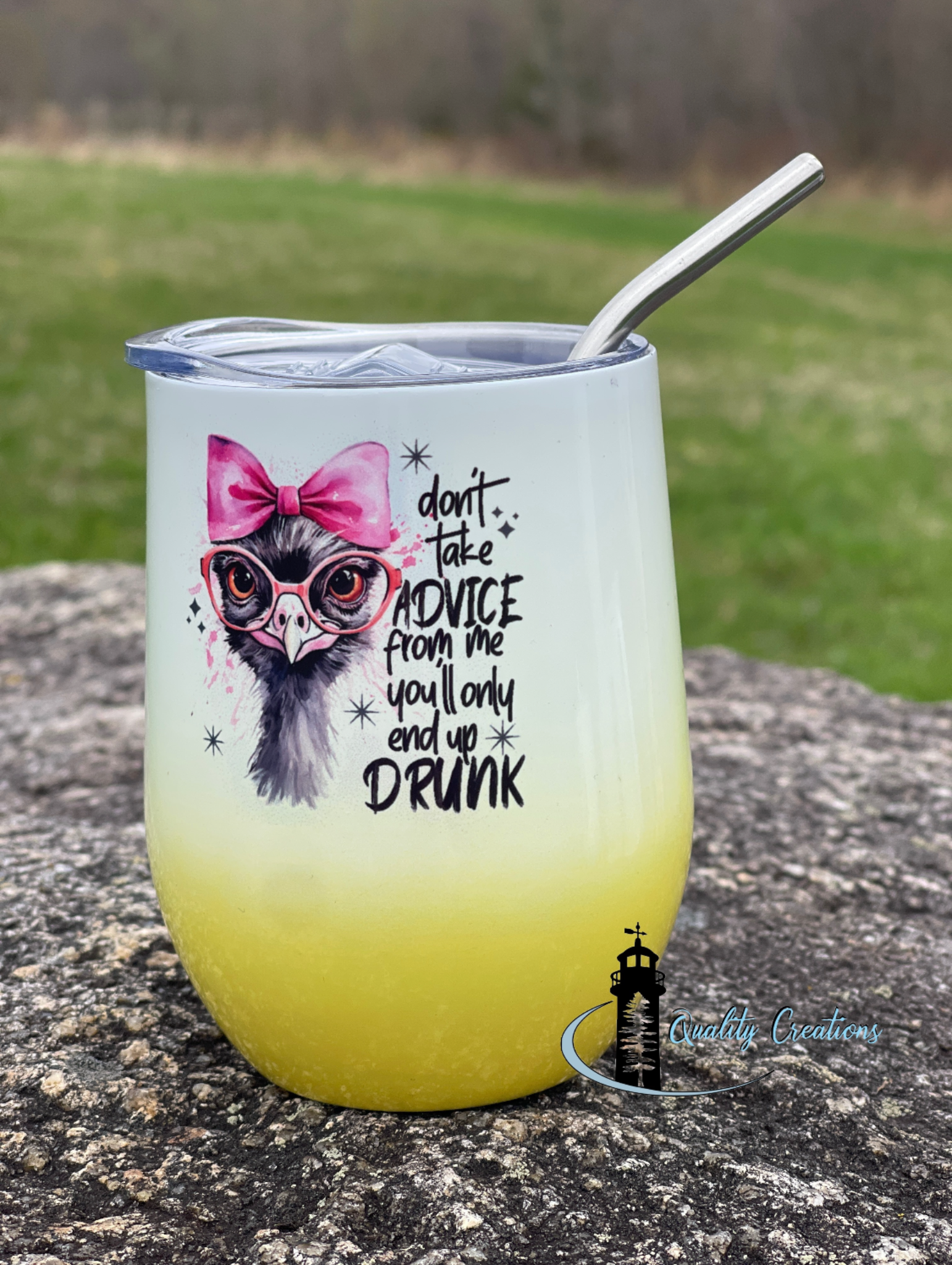 Gradient tumbler with a design and text on a stone surface with grass in the background
