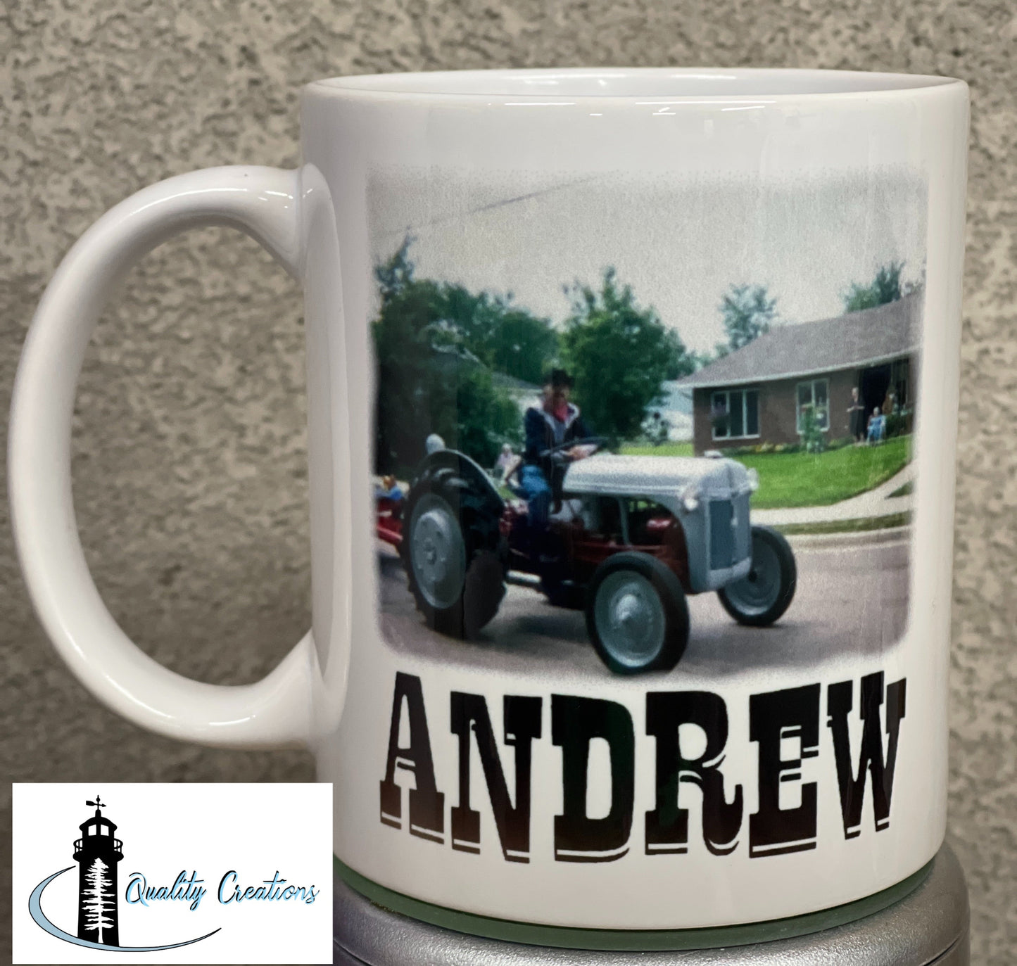 White mug featuring a custom photo of a man driving a vintage tractor with the name Andrew printed in bold western-style text, displayed on a grey surface