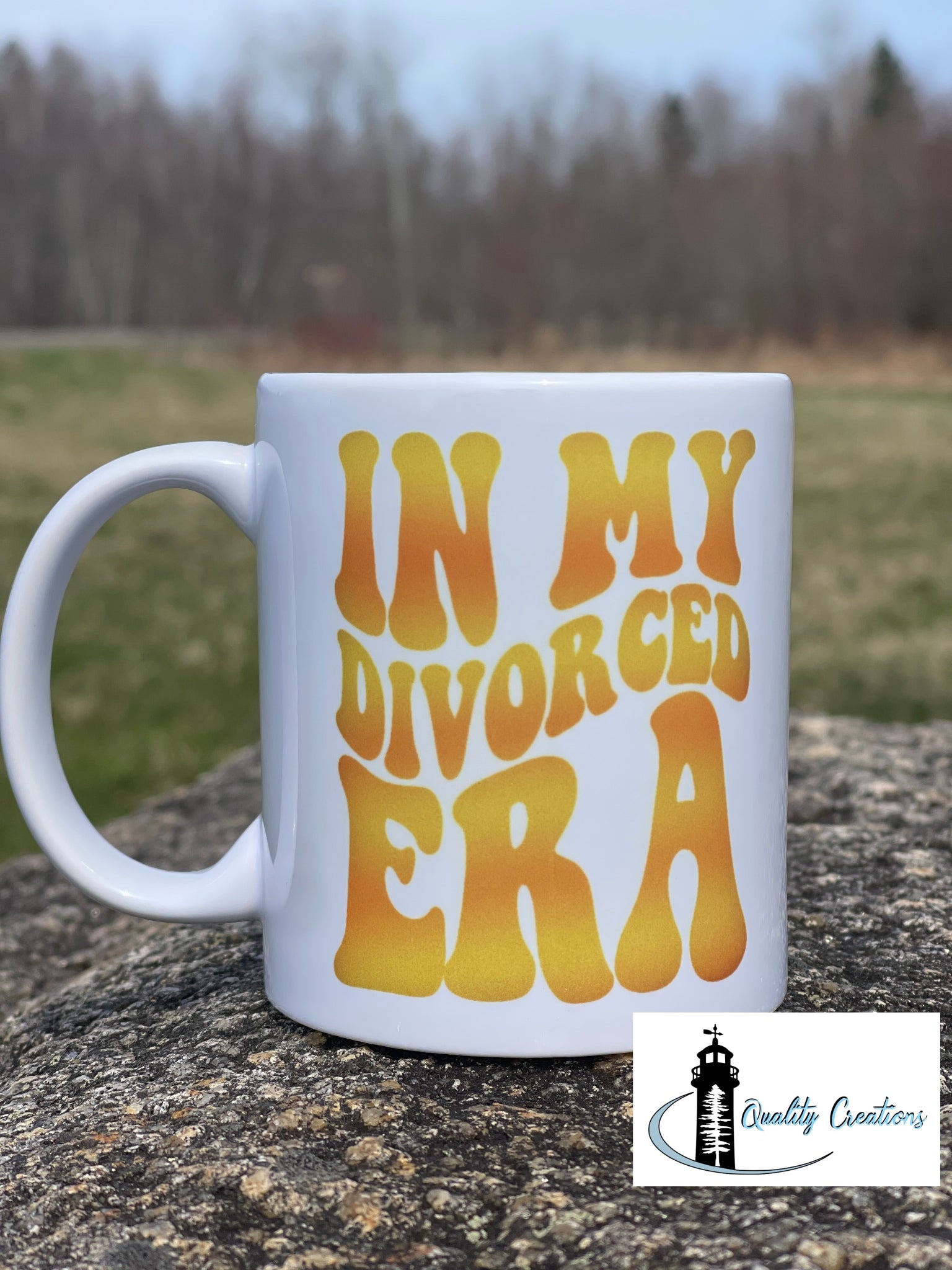 11oz White mug with bold retro yellow-orange text that reads In My Divorced Era, placed outdoors on a rock