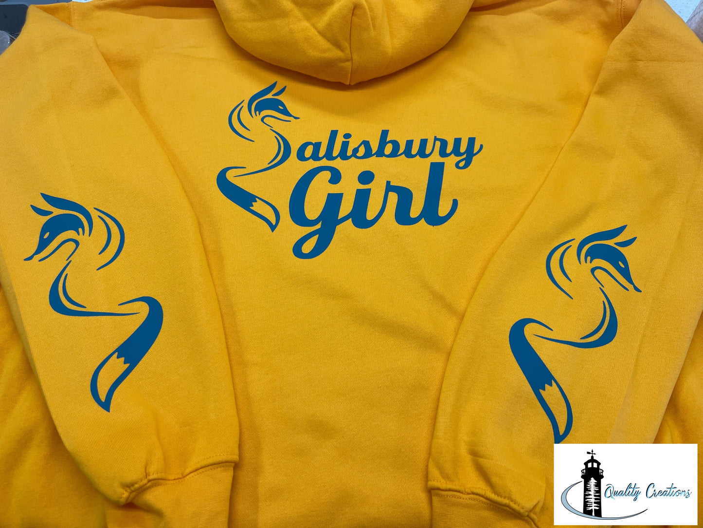 Bright gold Salisbury Girl pullover hoodie with royal blue text and fox sleeve graphics. Designed for proud locals in Salisbury, Moncton, Sussex, and Hampton, New Brunswick.
