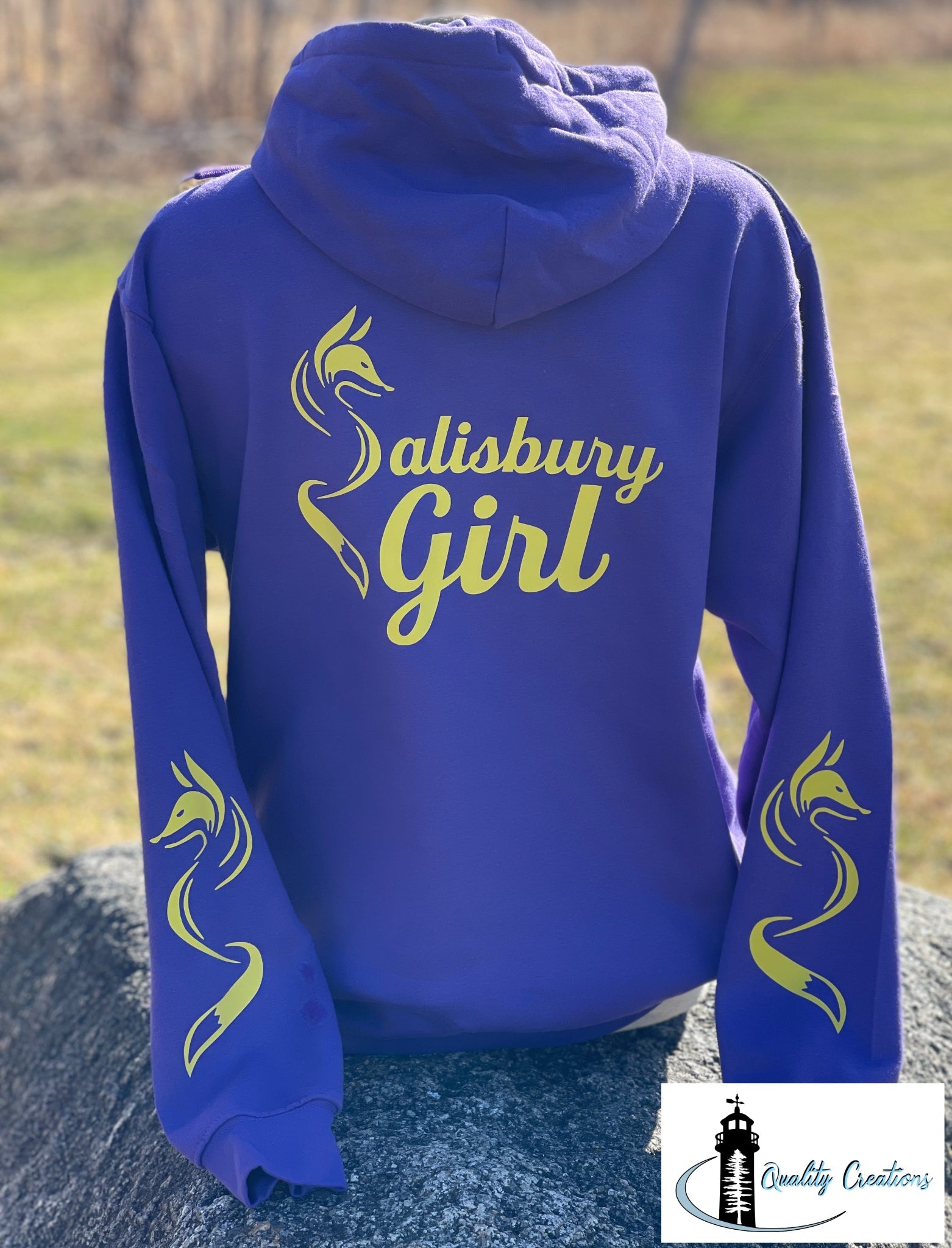 Purple Salisbury Girl pullover hoodie with yellow text and fox sleeve graphics. A cozy hometown design inspired by Salisbury, New Brunswick—home of the Silver Fox.
