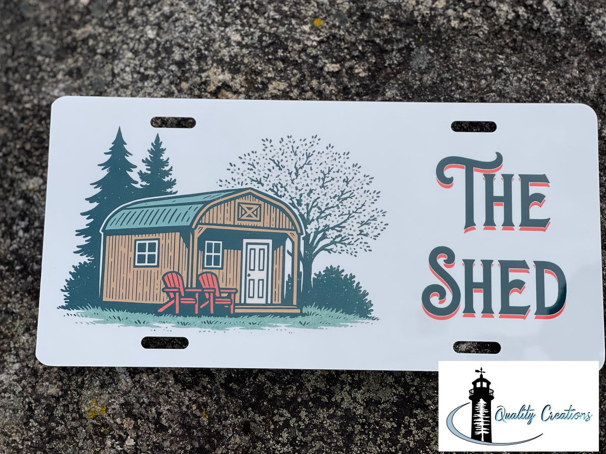 The Shed decorative license plate featuring a rustic backyard shed and Adirondack chairs, custom made by Quality Creations in New Brunswick