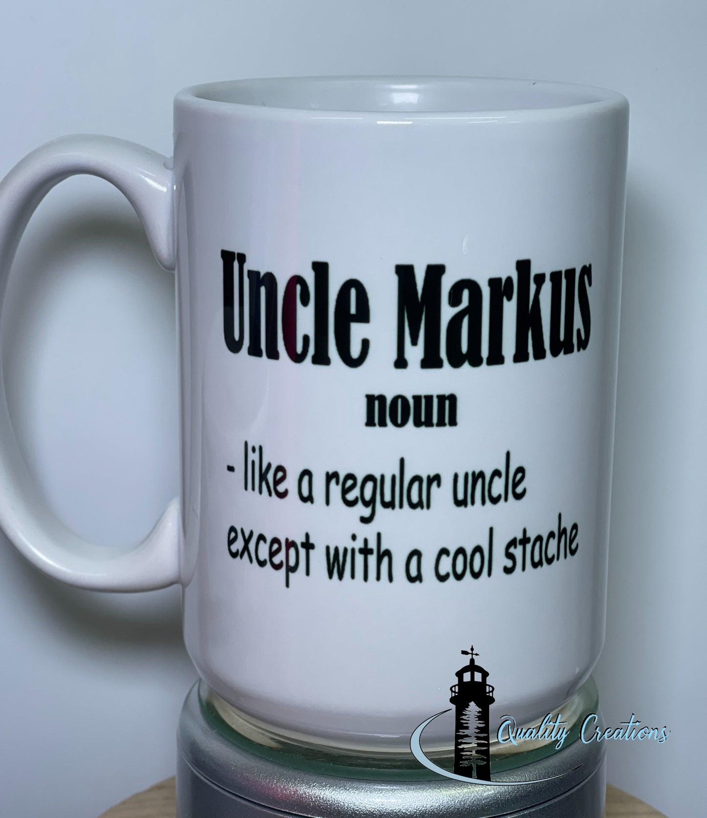 15oz White ceramic mug with bold black text that says: Uncle Markus, noun – like a regular uncle except with a cool stache, shown on a turntable with the Quality Creations logo