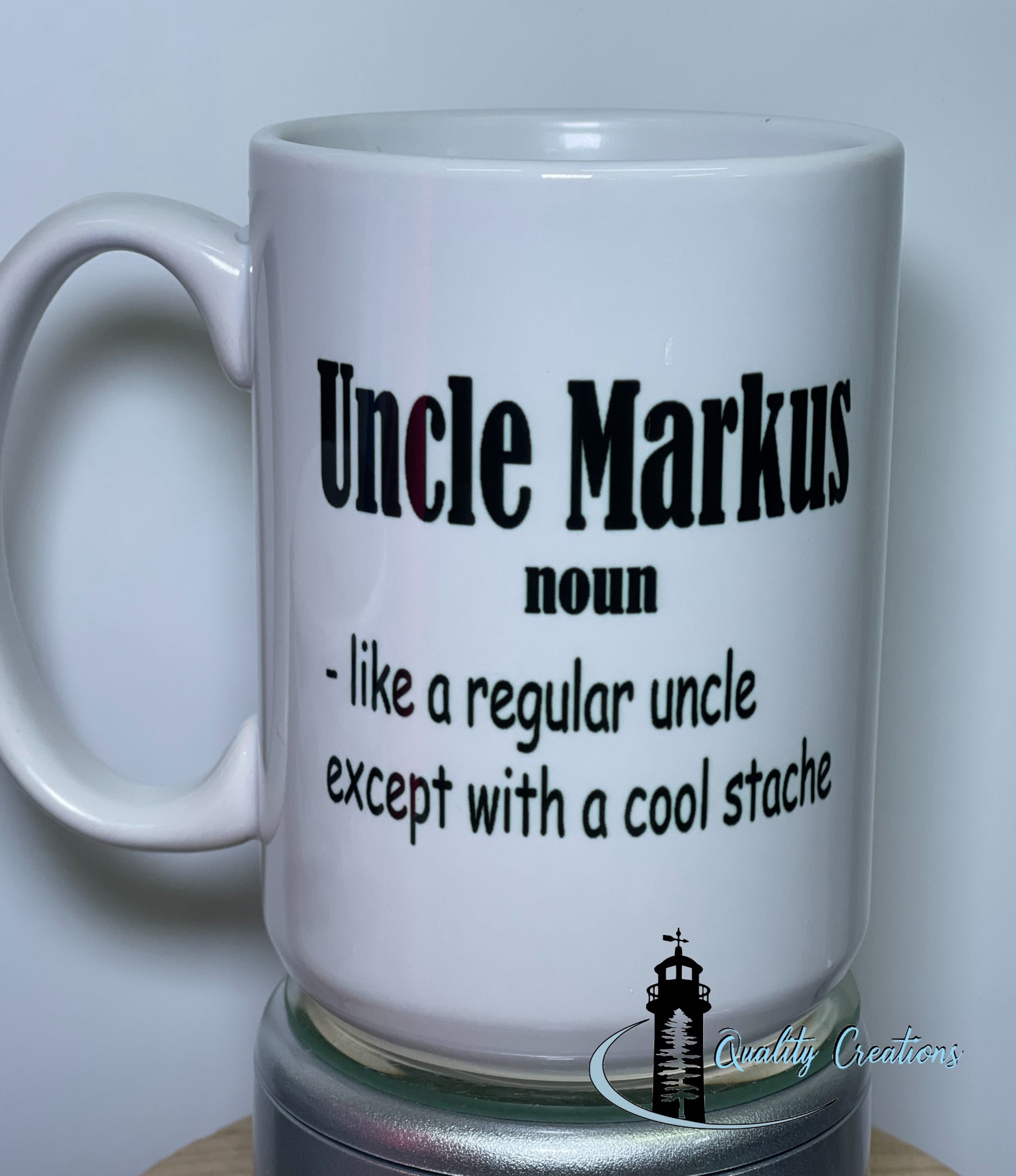 15oz White ceramic mug with bold black text that says: Uncle Markus, noun – like a regular uncle except with a cool stache, shown on a turntable with the Quality Creations logo